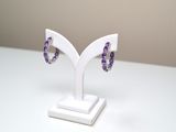 une paire de boucles d'oreilles violettes et blanches posées sur un présentoir blanc