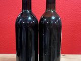 two bottles of wine sit on a wooden table in front of a red wall