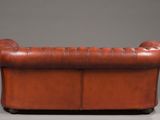 a brown leather sofa with a buttoned back and tufted arms
