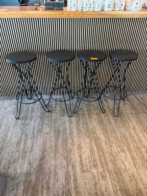 Trois tabourets noirs sont disposés devant un bar dont le mur est rayé.