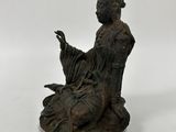 an old bronze statue of a woman sitting on a rock