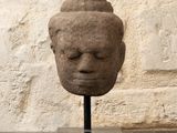 sculpture représentant une tête posée sur un socle devant un mur de pierre