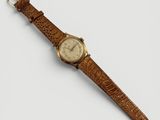gros plan d'une montre sur une surface blanche avec un bracelet marron