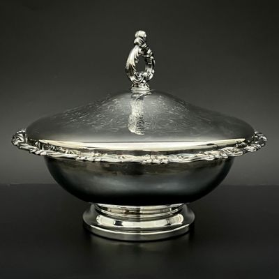 une image représentant un bol en argent muni d'un couvercle, posé sur une table