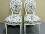 two white chairs with floral upholstered seats against a beige wall