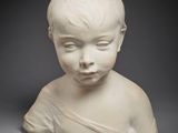un gros plan sur la statue blanche d'un enfant posée sur une surface grise