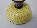 a yellow cracky vase with a black base on a white table