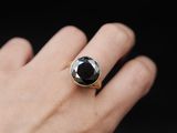 the hand is holding a ring with a black stone on it