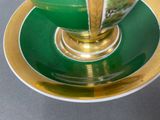 a green and gold cup and saucer sitting on a table