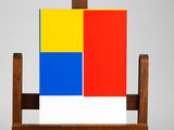 un chevalet en bois sur lequel est posé un tableau et un bloc de couleur rouge, jaune et bleu
