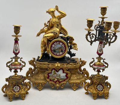 a gold clock sitting on top of a table next to three candelabs