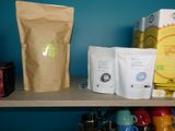a shelf with a bag of coffee, a bag of tea, a cup of coffee, and a bag of tea on it