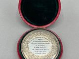 une image représentant une petite boîte rouge contenant une médaille en argent