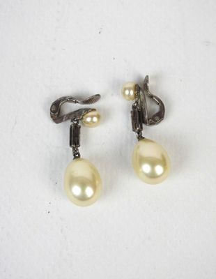 une paire de boucles d'oreilles en perles et diamants posées sur un fond blanc