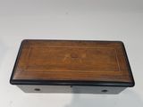 a small wooden box with a black lid and a gold emblem on it