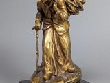 une statue en bronze représentant une vieille femme avec une canne, posée sur un socle en marbre