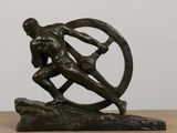 bronze statue of a man holding a wheel on a wooden table