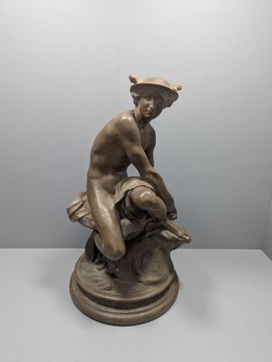 statue en bronze représentant un garçon assis sur un rocher, coiffé d'un chapeau