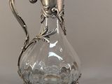 a glass pitcher with a metal handle on a table
