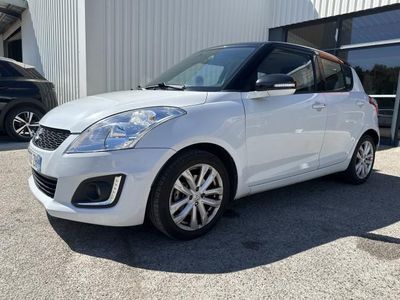 Une Suzuki Swift blanche est garée devant un immeuble.