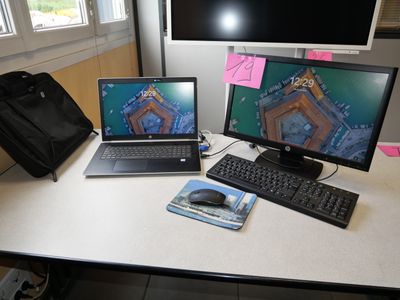 two laptops and a keyboard on a desk with a bag
