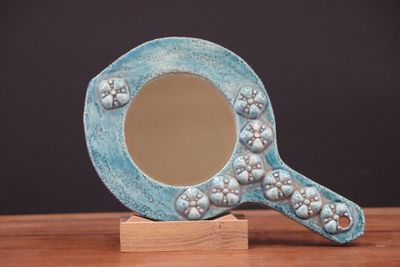 un miroir bleu posé sur un socle en bois, lui-même posé sur une table