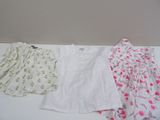 Trois vêtements pour bébé sont alignés sur une table blanche