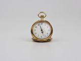 une image représentant une petite montre de poche en or posée sur une surface blanche