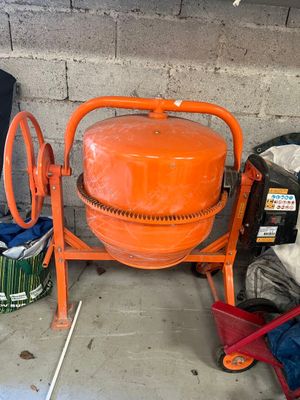 une bétonnière orange à côté d'un seau de ciment