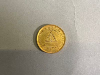 une pièce d'or sur laquelle est gravé un triangle, posée sur une table