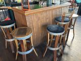 trois tabourets en bois disposés devant un bar, avec un tableau noir accroché au mur