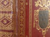 un vieux livre rouge aux tranches dorées, orné d'un blason sur la couverture
