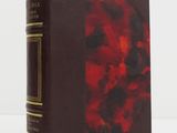 an old book with a red cover sitting on top of a white table