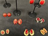 several pairs of red and gold earrings are displayed on a black table