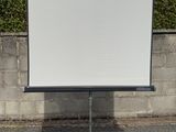 un écran de projection monté sur un trépied devant un mur de pierre