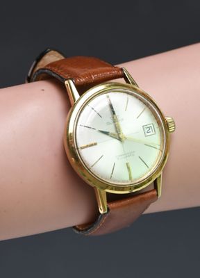 a watch on a woman ' s wrist with a brown strap