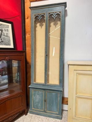 une armoire haute avec une porte vitrée, à côté d'une commode