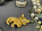 a necklace with a cat on it next to a bunch of pearls