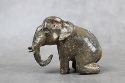 une statue d'éléphant assis par terre, la trompe tendue