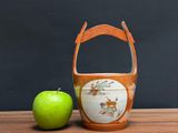 a green apple next to an orange vase on a wooden table