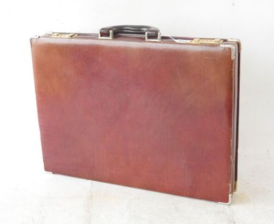 une valise en cuir marron posée sur une surface blanche, sur fond blanc