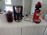a red coffee maker on the counter next to a roll of toilet paper