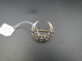 a gold and diamond crescent broochle on a black surface