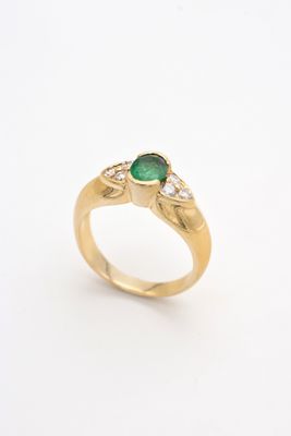 gros plan d'une bague en or avec une pierre verte et des diamants