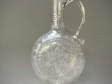 un vase en verre transparent muni d'une poignée en argent, posé sur une table
