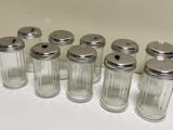 six glass jars with silver lids are lined up on a white surface
