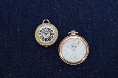 two different types of pocket watches on a blue cloth