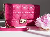 a pink purse sitting on a table next to a pink flower