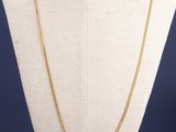 un collier en or avec un pendentif carré autour du cou d'un mannequin