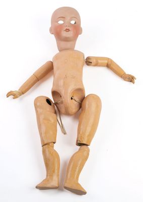une poupée en bois assise sur une surface blanche, tenant une paire de ciseaux